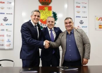Representantes institucionales y deportivos estrechándose la mano durante la firma del acuerdo para celebrar la Copa del Rey de Balonmano en Santander, con el escudo de la RFEBM y logotipos de patrocinadores al fondo.