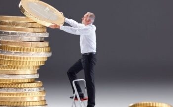 Hombre subido a una escalera colocando una moneda gigante sobre una gran pila de monedas apiladas, simbolizando el ahorro, la inversión o la planificación financiera.
