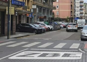 Señal horizontal de Zona de Bajas Emisiones (ZBE) pintada en una calle de Torrelavega, con coches aparcados, tráfico y edificios residenciales, en el contexto de la petición de APEMECAC de una moratoria en su aplicación.